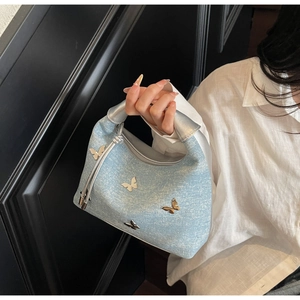 Detail of light blue denim handbag featuring silver butterfly charms and metallic handles