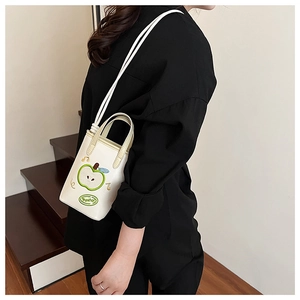 White bucket bag with green apple embroidery and long strap shown on model's shoulder