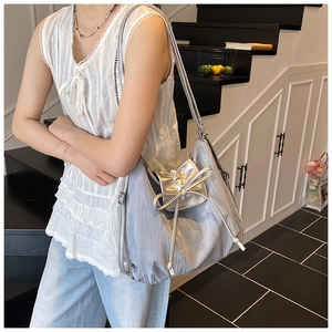 Silver wrinkled tote bag with drawstring bow detail worn by a model in a modern indoor setting