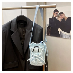 Close-up of light blue drawstring crossbody bag with pleated texture and zipper pocket