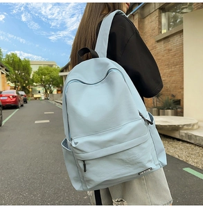 Light blue minimalist backpack shown on model in outdoor setting for size scale