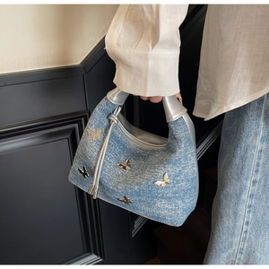 Detail of denim handbag with metallic butterfly charms and silver leather handle held by model