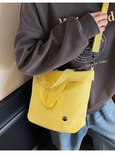 Yellow pleated canvas bucket bag with wide shoulder strap shown on a casual model