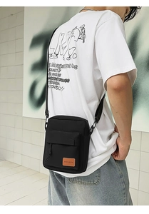 Close-up of black canvas crossbody phone bag with adjustable strap on white t-shirt