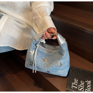Detail of light blue denim handbag with silver bow charms and shiny leather handle