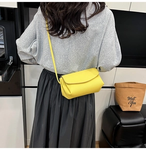 Détail d'un sac bandoulière en cuir jaune vif sur un mannequin dans une cuisine moderne