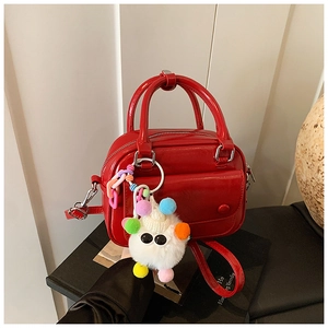 Detail of red patent leather boston bag with colorful plush monster charm on black stand