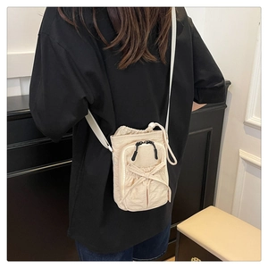 Detailed view of a cream crossbody phone bag with drawstring and decorative bow on a model
