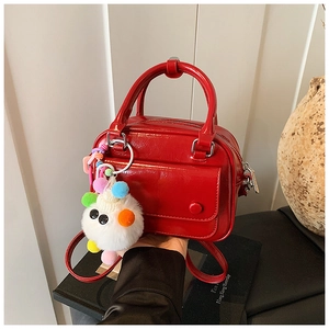 Detail view of red glossy patent leather mini bag with white fuzzy charm and metal zipper