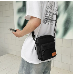 Street style view of a black canvas crossbody bag featuring a leather logo patch and zip
