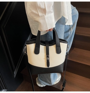 Close-up of a high-capacity black and white bucket bag with pebble texture on wooden stairs