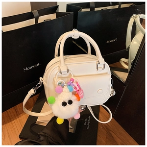 Detailed view of white patent leather handbag with plush monster charm on mirror background