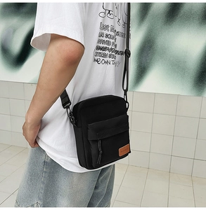 Detail of black crossbody nylon bag featuring a brown leather logo tag and woven strap
