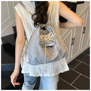 Silver metallic drawstring backpack with bow detail shown on a model in a stairwell