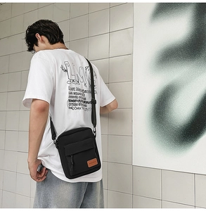 Close-up of black canvas crossbody bag with adjustable strap and leather logo detail