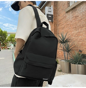 Outdoor street view of a large black minimalist canvas backpack worn by a male student