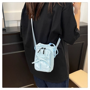 Light blue nylon crossbody bag with drawstring closure and black bow detail shown on model