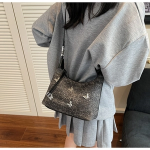 Detail shot of a grey glitter shoulder bag with five silver butterfly appliques on a model