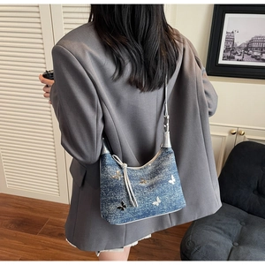 Détail du sac à épaule en jean bleu à paillettes et papillons porté par un mannequin