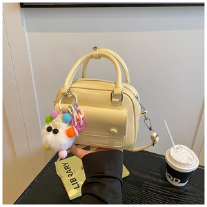 Detail of a beige patent leather pillow bag with a plush character charm and handle