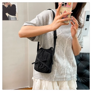 Detail of black mini crossbody bag featuring a bow decoration and adjustable strap on a model
