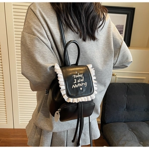 Detail of black PU leather backpack with white frill trim and embroidered quote on the back