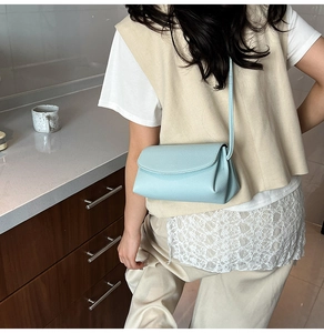 Petit sac bandoulière bleu clair en cuir grainé porté par un mannequin en intérieur