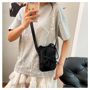Detail of black nylon crossbody bag featuring stylish bow drawstring and slim shoulder strap