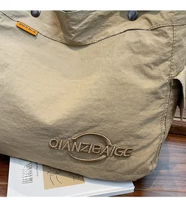Dettaglio ravvicinato della borsa tote beige con etichetta arancione e logo ricamato