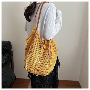 Detail of yellow knit hobo bag with colorful sequins and brown leather straps on model