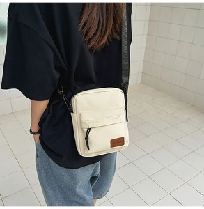 Close-up of beige canvas crossbody bag with adjustable strap worn by a model