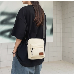 Detail of a minimalist cream canvas crossbody bag with a wide strap and zip pocket