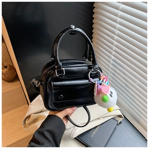 Detail of black glossy leather handbag featuring double handles and heart charm decoration