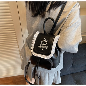 Close-up of black leather backpack featuring white ruffled edges and embroidered text detail