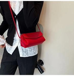 Détail du sac bandoulière rouge avec texture litchi et rabat porté par un mannequin