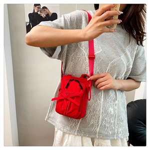 Detail of red crossbody bag with bow accent, double zippers, and adjustable strap