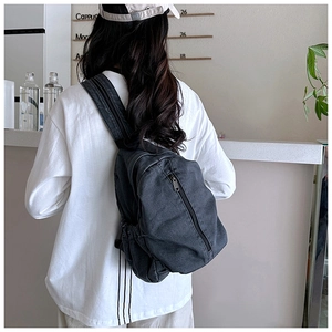 Détail d'un grand sac à dos en jean gris foncé porté sur un t-shirt blanc décontracté