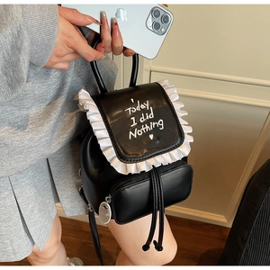 Detail of black mini backpack featuring white ruffle edges and heart embroidery