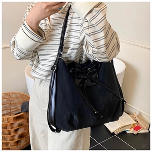 Chic black tote bag with satin drawstring bow detail shown on a model in a cozy indoor setting