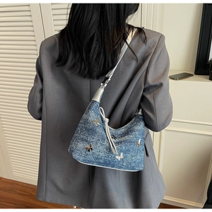 Denim shoulder bag with silver butterfly charms shown on model against a white wall
