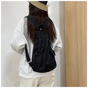 Detail eines schwarzen Denim-Rucksacks mit drei Taschen und Kordelzug an einem Model