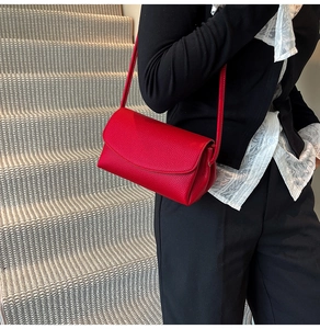 Sac à bandoulière en cuir rouge motif litchi porté sur un mannequin en blazer noir