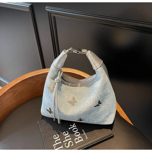 Detailed shot of light blue denim handbag featuring silver metal butterfly embellishments