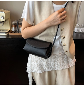 Vue détaillée d'un sac bandoulière noir en cuir grainé dans un décor de café