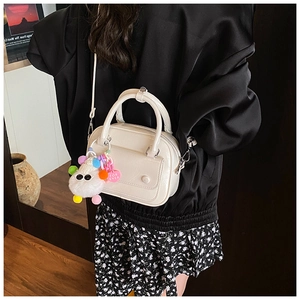 Detail of cream leather pillow bag featuring cute plush charm and elegant hand straps