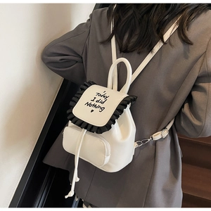 Detail of a beige mini backpack with black ruffle trim and playful slogan on the flap