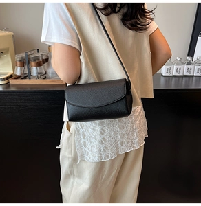 Détail d'un sac bandoulière en cuir grainé noir porté par un mannequin dans un café