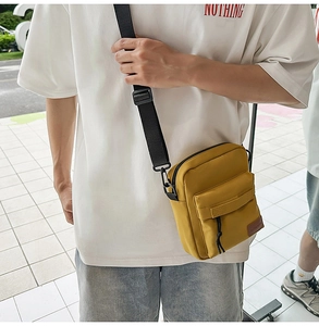 Detail of yellow canvas crossbody phone bag with black adjustable strap and front pocket