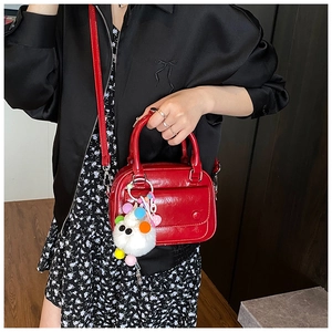 Red glossy pillow bag with plush heart charm shown in a crossbody style on model