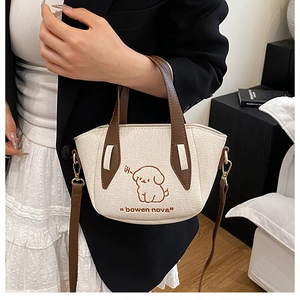 Detail of beige textured handbag with brown leather strap and puppy embroidery